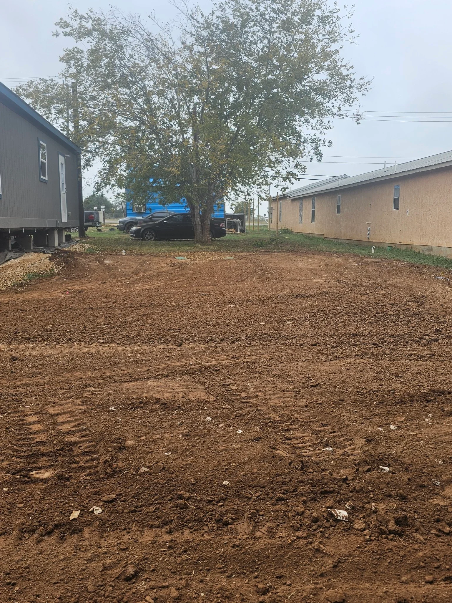 Freshly excavated and graded residential driveway site with compacted earth and mature trees